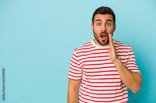 Young caucasian man isolated on blue background shouts loud, keeps eyes opened and hands tense.