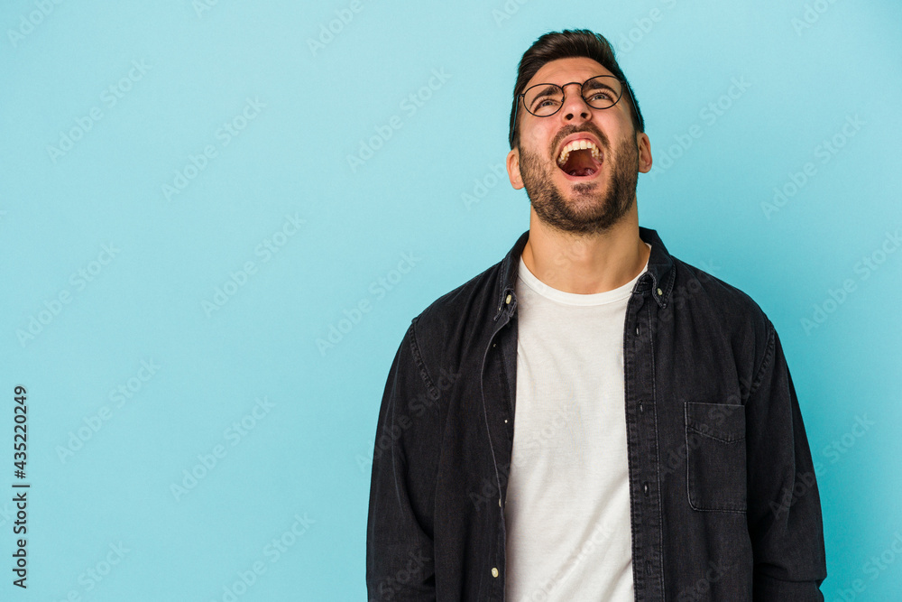 Obraz premium Young caucasian man isolated on blue background shouting very angry, rage concept, frustrated.