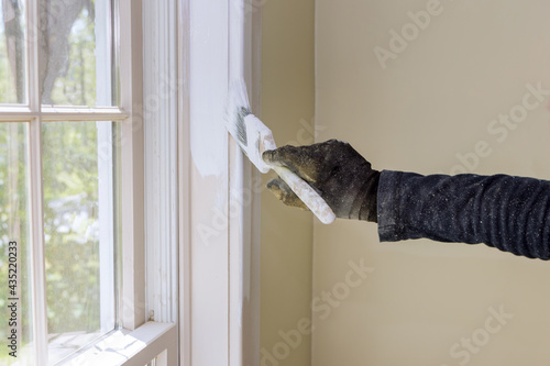 Fototapet Home renovation in the handyman paints with a paint brush a window molding frame