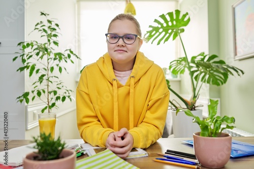 Portrait of girl 12, 13 years old in yellow sweatshirt with glasses looking at the camera photo