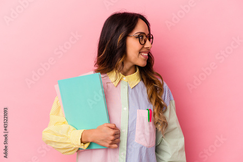 Young student mexican woman isolated on pink background looks aside smiling, cheerful and pleasant.
