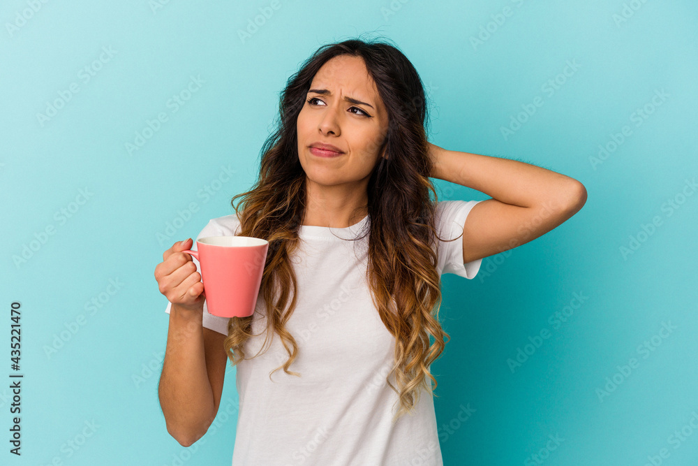 Young mexican woman holding a mug isolated on blue background touching back of head, thinking and making a choice. Young mexican woman holding a mug isolated on blue background touching back of head, thinking and making a choice.