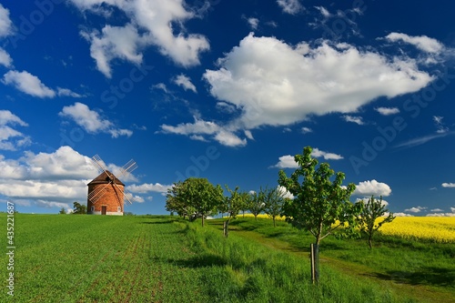 Beautiful spring landscape with blue sky, sun, clouds and old windmill.