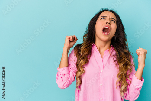 Young mexican woman isolated on blue background raising fist after a victory, winner concept.