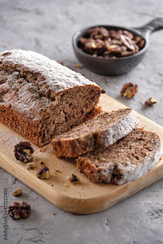 Delicious and flavorful banana cake with nuts and chocolate on a wooden board with a cup of coffee on a gray background