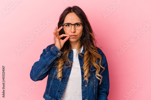Young mexican woman isolated on pink background with fingers on lips keeping a secret. © Asier
