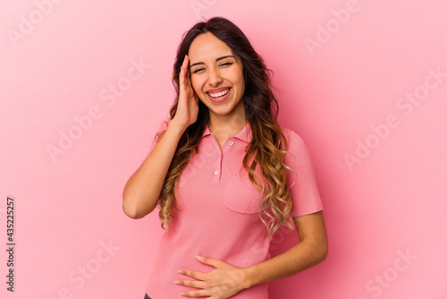 Young mexican woman isolated on pink background laughs happily and has fun keeping hands on stomach.