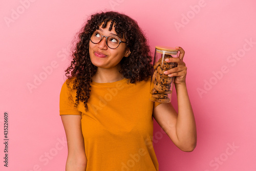 Papier peint Young mixed race woman holding a cookies jar isolated on pink background dreamin