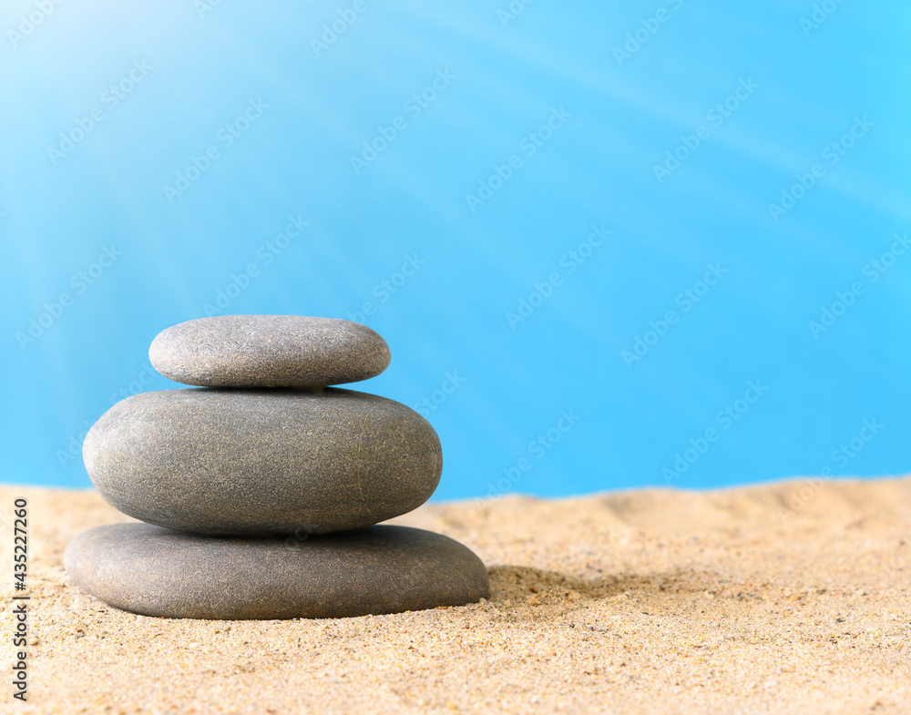 Summer composition with natural stones and sun rays on sand on a blue background Summer composition with natural stones and sun rays on sand on a blue background