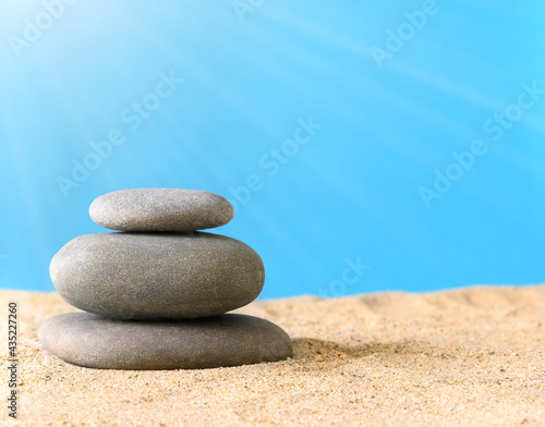 Summer composition with natural stones and sun rays on sand on a blue background