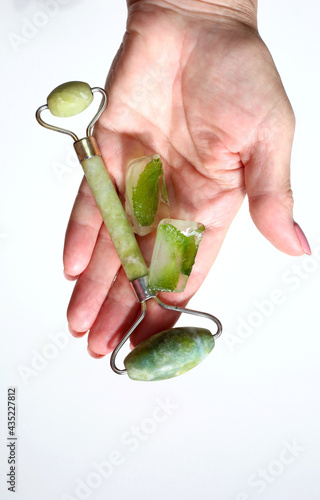 Fototapeta Naklejka Na Ścianę i Meble -  Hand holding green face roller and ice cubes. Derma roller for skin care.