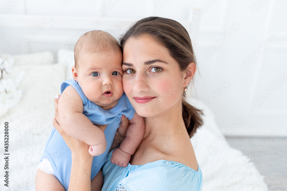 a young mother with a newborn baby gently embraces him at home on the bed, the concept of a happy family and birth a young mother with a newborn baby gently embraces him at home on the bed, the concept of a happy family and birth