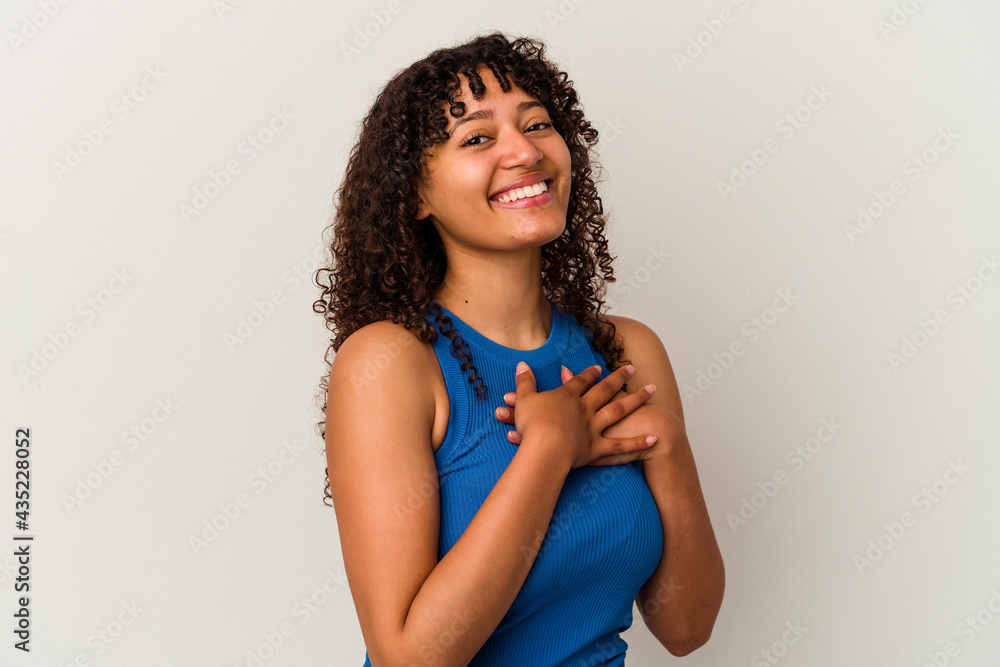 Young mixed race woman isolated on white background has friendly expression, pressing palm to chest. Love concept.