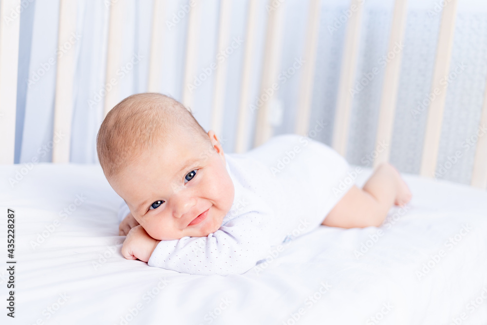 smiling newborn baby on tummy in crib on cotton bed at home, healthy baby concept smiling newborn baby on tummy in crib on cotton bed at home, healthy baby concept