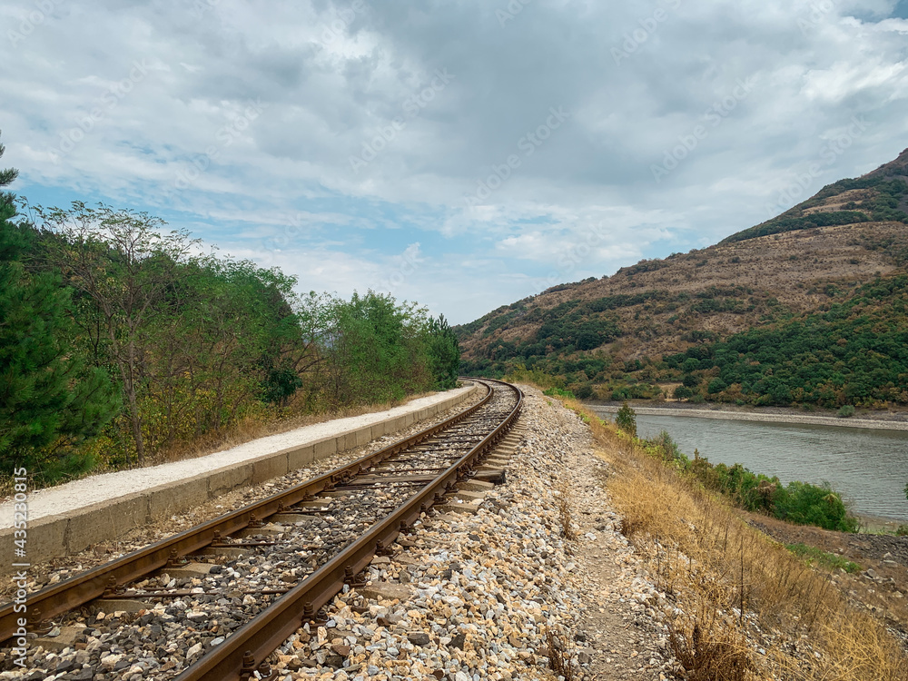 Fototapeta premium Old mountain railroad track leading between forest and lake.