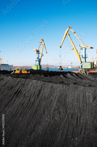 Huge amount of coal in the Murmansk commercial seaport. Loading of coal by buckets (grabs) of portal cranes into the holds of a dry cargo ship in the seaport