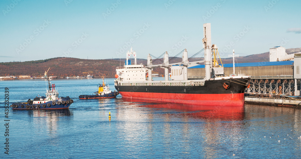 Kola Bay, Murmansk Commercial Sea Port. Tugs are engaged in mooring bulk carriers to the mooring walls, and then unmooring them