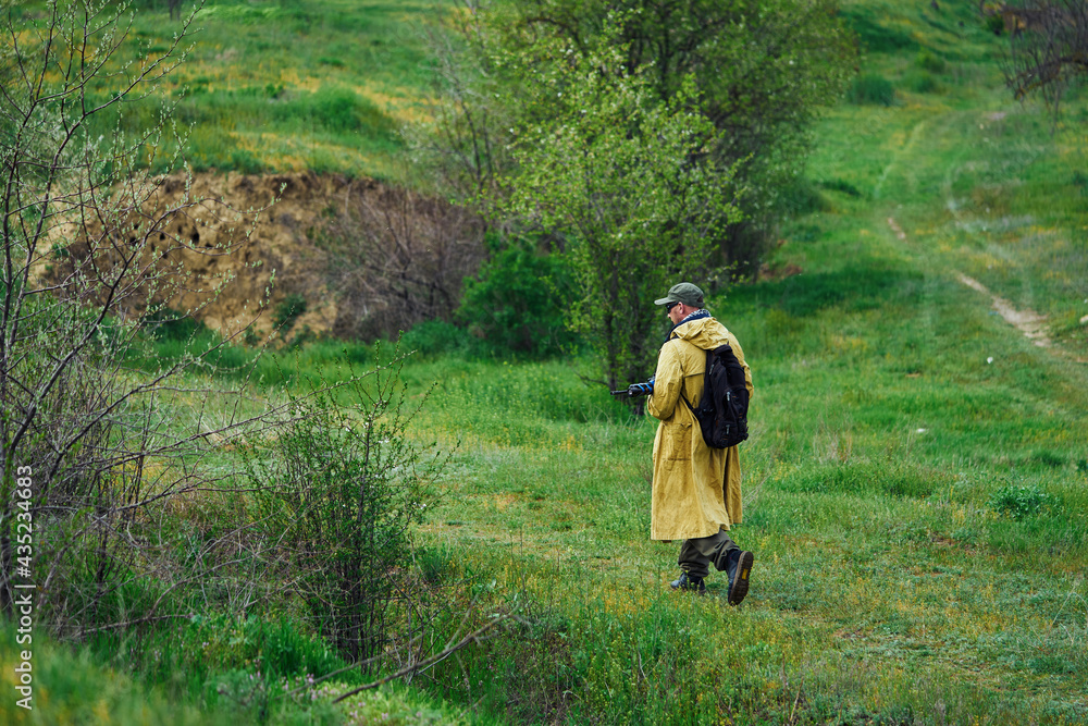 An airsoft player in a yellow raincoat walks with a weapon in his hands An airsoft player in a yellow raincoat walks with a weapon in his hands