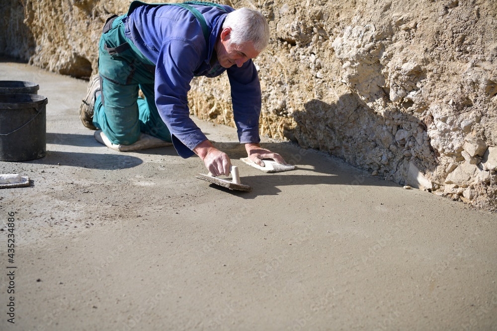 The mason on his knees coats the concrete floor with cement The mason on his knees coats the concrete floor with cement