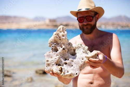 Tablou pe pânză Bearded man holding big part of coral in his hands on the background of Red sea, Egypt
