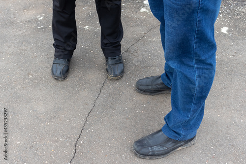 men's and women's feet stand on the broken asphalt. women's legs in black trousers, men's legs in blue jeans. only the legs are in the frame