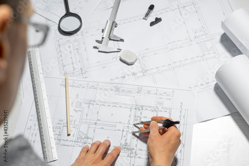The hands of a professional architect draw a sketch of a design project with a pencil. Work table of a civil engineer creating blueprints for a building.