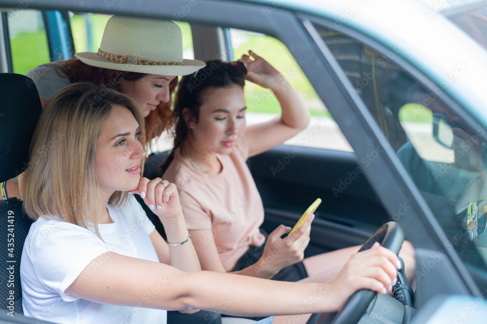 Three happy girlfriends go on a trip. Women Ride in the car, look at the phone and laugh. Three happy girlfriends go on a trip. Women Ride in the car, look at the phone and laugh.