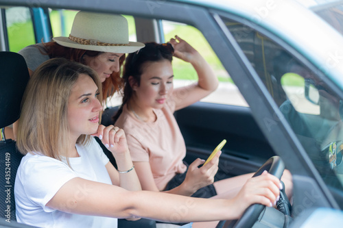 Three happy girlfriends go on a trip. Women Ride in the car, look at the phone and laugh. © Михаил Решетников