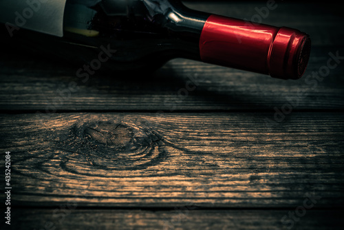 Bottle of red wine lying on an old wooden table. Close up view, focus on the bottle of red wine © Georgii Shipin