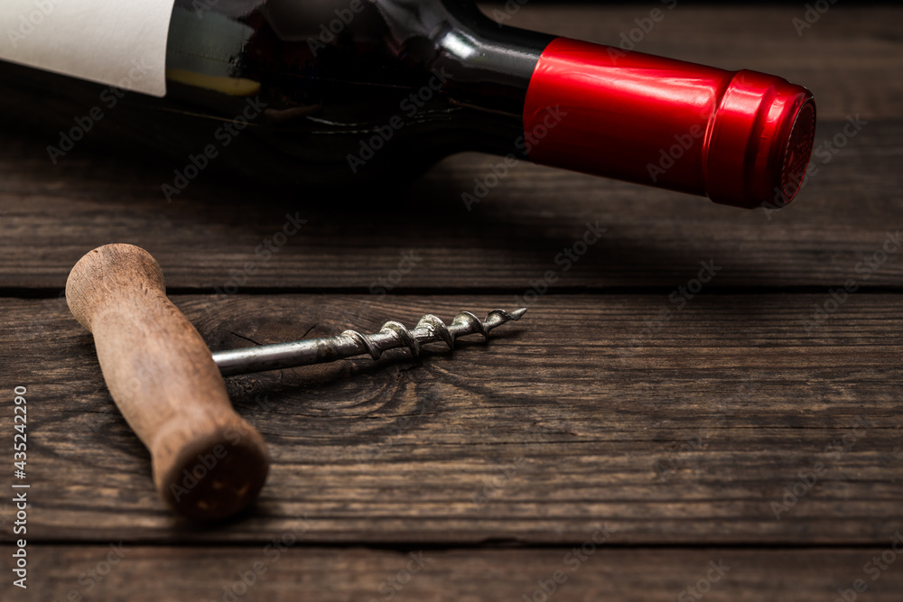 Bottle of red wine and corkscrew lying on an old wooden table. Close up view, focus on the corkscrew