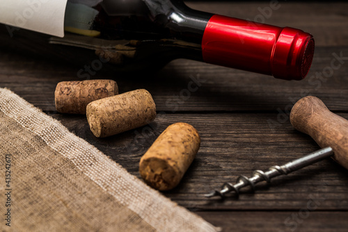 Bottle of red wine and piece of canvas with corkscrew and corks lying on an old wooden table. Close up view, focus on the bottle of red wine