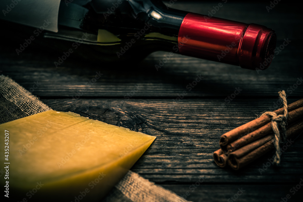 Bottle of red wine with a piece of parmesan and cinnamon sticks on an old wooden table. Close up view, focus on the bottle of red wine