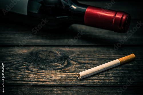 Bottle of red wine and cigarette lying on an old wooden table. Close up view, focus on the cigarette