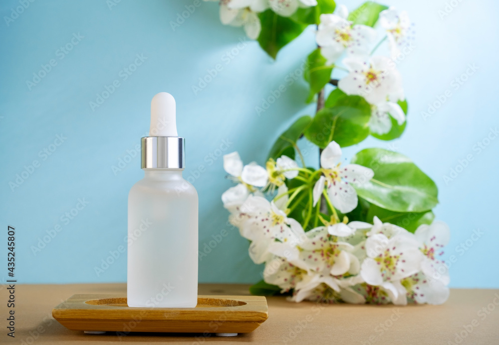 Blank transparent beauty serum dropperon a blue background with blooming apple tree branch. Beauty care concept,selective focus. Blank transparent beauty serum dropperon a blue background with blooming apple tree branch. Beauty care concept,selective focus.