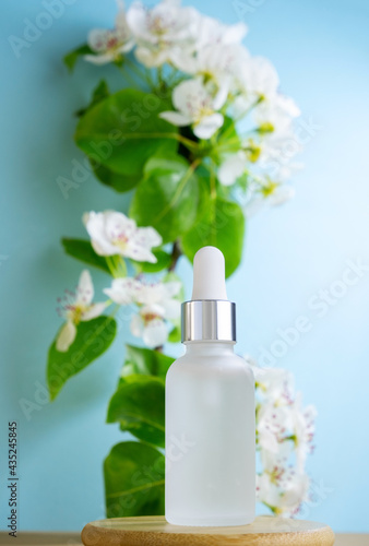 Blank transparent beauty serum dropperon a blue background with blooming apple tree branch. Beauty care concept selective focus.