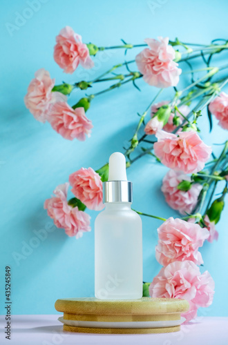 Blank transparent beauty serum dropperon a blue background with blooming pink carnation flowers. Beauty care concept advertisment poster.