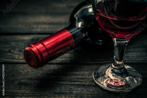 Bottle of red wine with a glass of red wine on an old wooden table. Close up view, focus on the bottle of red wine