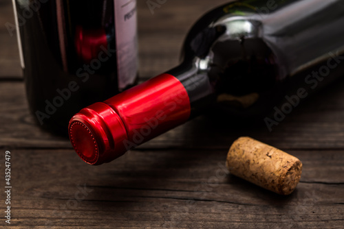 Two bottles of red wine and cork lying on an old wooden table. Close up view, focus on the bottle of red wine