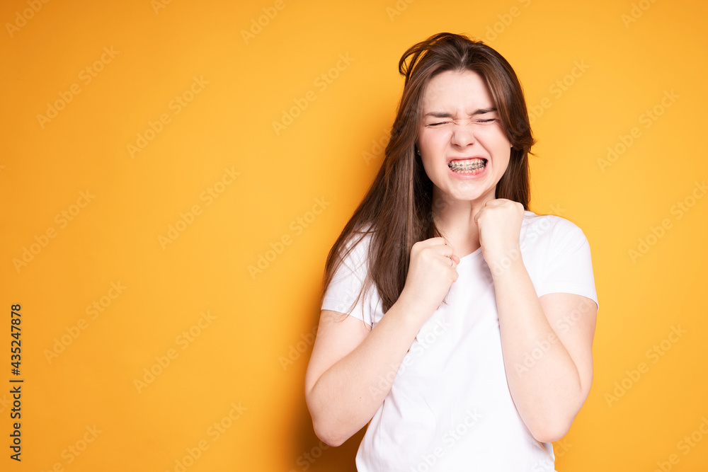 A beautiful girl pretends to hit her jaw with her fists because of a pain in her teeth. Isolated on yellow background A beautiful girl pretends to hit her jaw with her fists because of a pain in her teeth. Isolated on yellow background