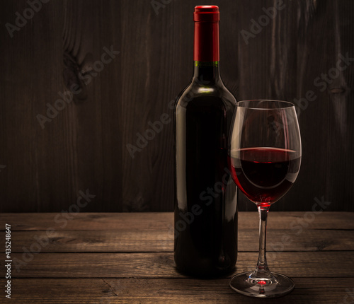 Bottle of red wine with a glass of red wine on an old wooden table