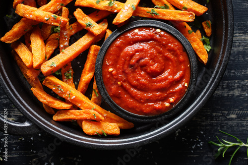 Sweet potato fries with spicy tomato sauce served on a cast iron dish on a dark table close up view. A healthy alternative photo