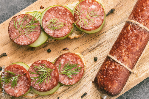 salami sausage stick and rye bread sandwiches with smoked sausage and vegetables on cutting board, harmful fast food, fatty not healthy food, top view