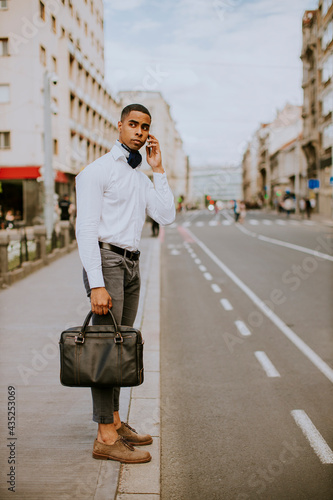 Young African American businessman using a mobile phone while waitng for a taxi on a street photo