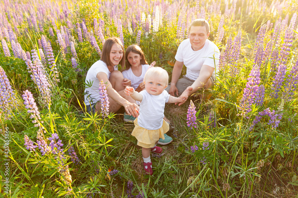 Fototapeta premium Happy family mother father embracing kids outdoor. Woman man baby child and teenage girl sitting on summer field with blooming flowers background. Happy family mom dad and daughters playing on meadow.