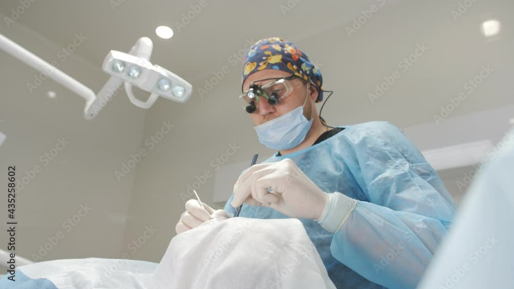 Surgery in a dental clinic. The dentist surgeon stitches the wound in