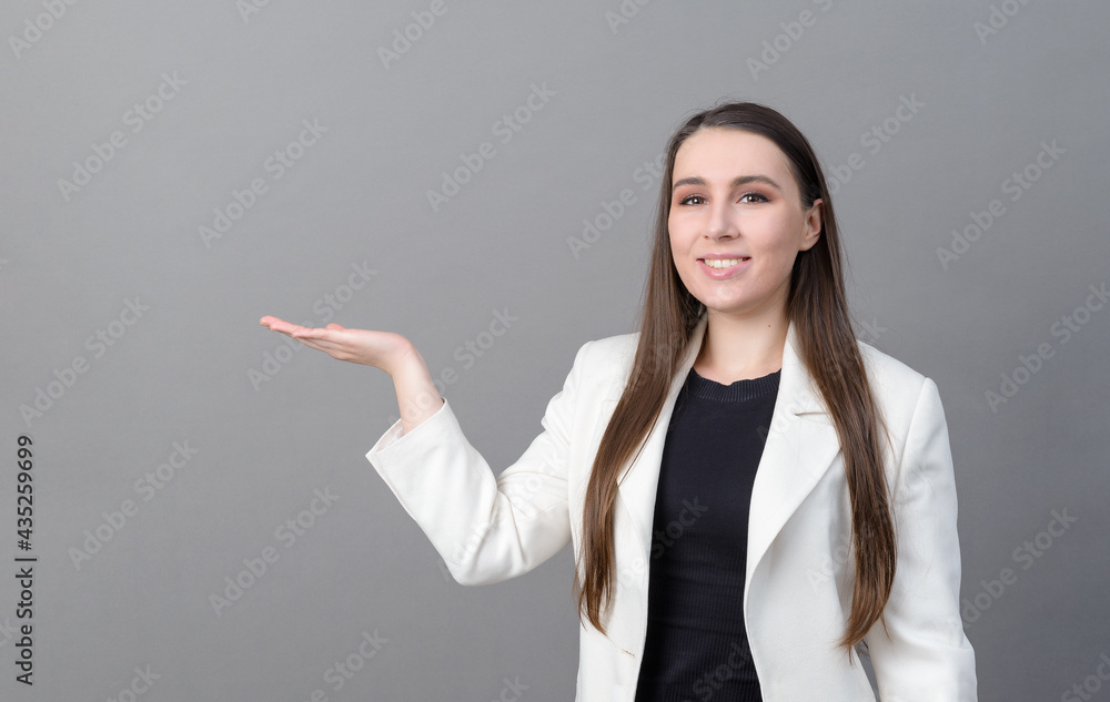 young woman with long hair in a white jacket points to the side on a gray young woman with long hair in a white jacket points to the side on a gray