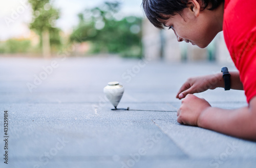 Schilderij op canvas Closeup of a caucasian boy playing with a spinning top in the park