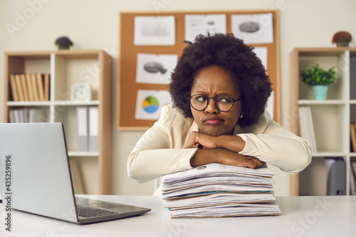 Φωτογραφία Lazy displeased fatigue young frowning african american woman worker employee keeping chin on paper stack folder pile sitting at table in office