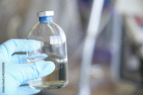 Researcher hand wearing gloves holding a bottle for anaerobic cultures, with cap and septum. Anaerobic media.