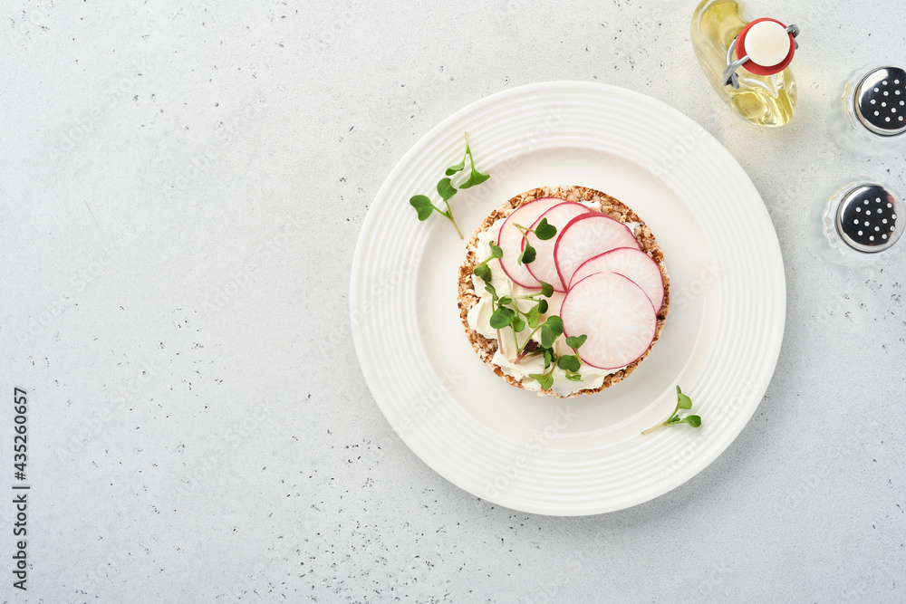 Crispy buckwheat bread cake gluten free with cream cheese, red radish and microgreen for healthy breakfast on grey stone background. View from above. Concept vegan and healthy eating. Crispy buckwheat bread cake gluten free with cream cheese, red radish and microgreen for healthy breakfast on grey stone background. View from above. Concept vegan and healthy eating.